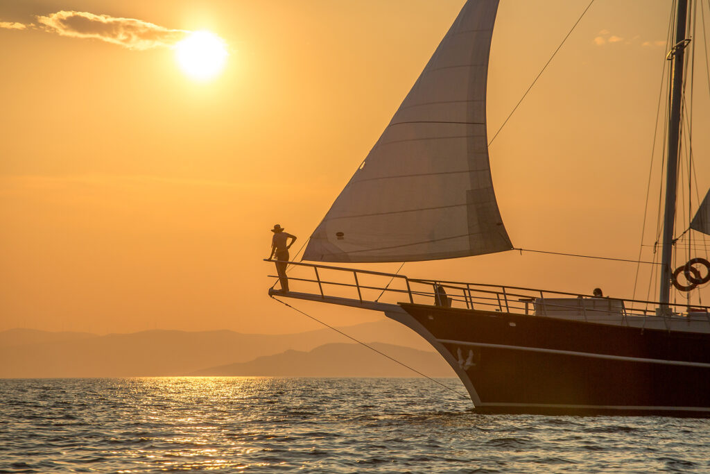 Person standing on the front bow of a luxury yacht at sunset, looking out at the golden horizon in Croatia.