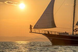 Person standing on the front bow of a luxury yacht at sunset, looking out at the golden horizon in Croatia.
