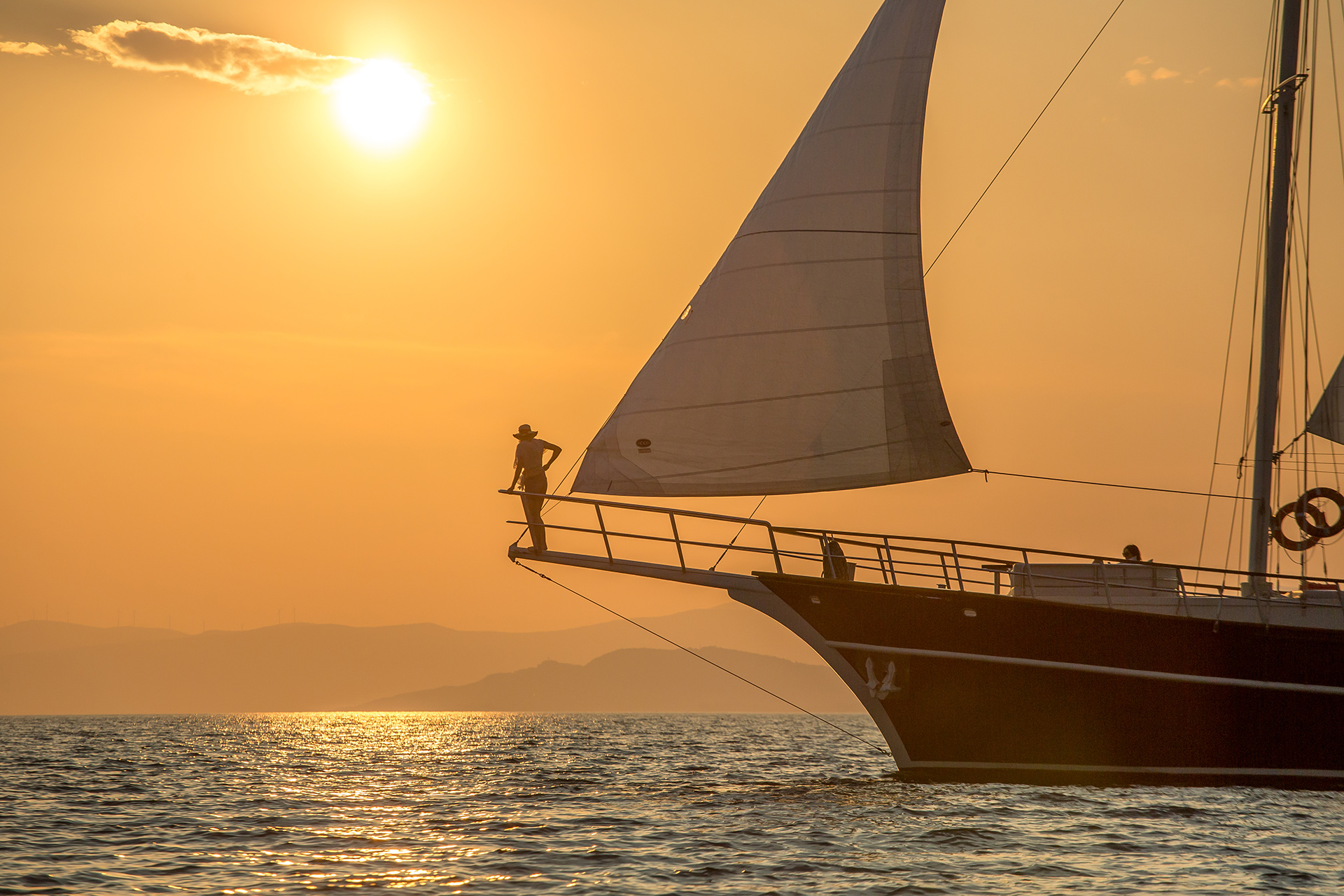Person standing on the front bow of a luxury yacht at sunset, looking out at the golden horizon in Croatia.