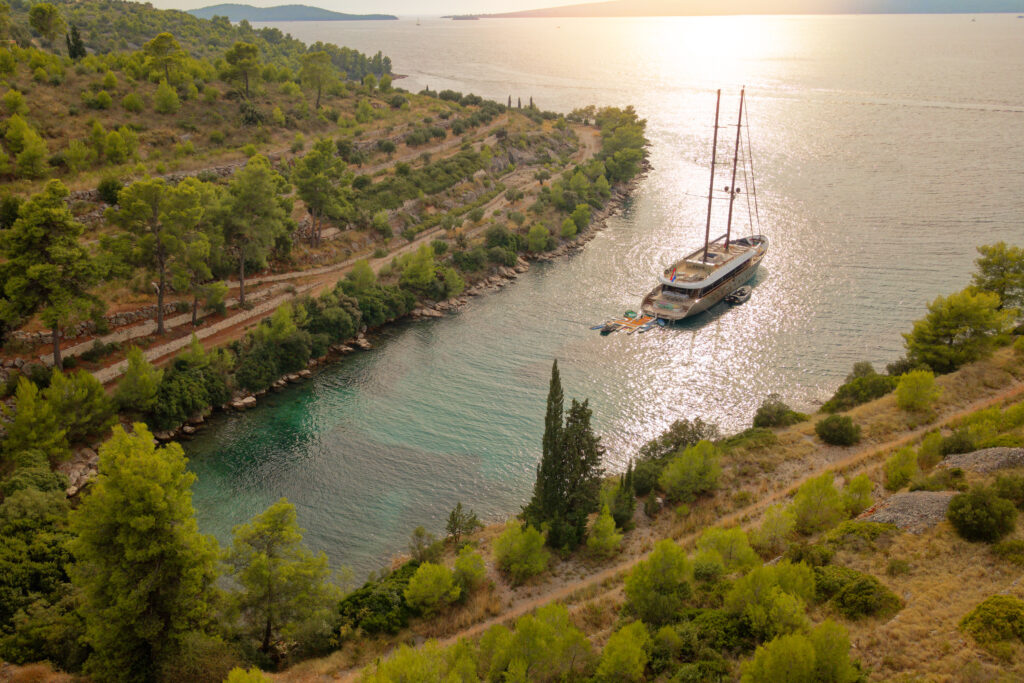 A modern luxury sailing yacht anchored in a secluded, turquoise Adriatic bay surrounded by pine-covered hills in Croatia.