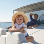 A father smiling at his 4-year-old daughter enjoying a sailing trip on a luxury yacht.