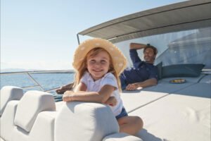 A father smiling at his 4-year-old daughter enjoying a sailing trip on a luxury yacht.